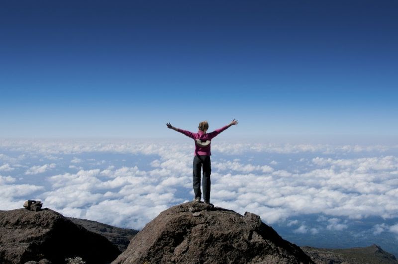 Standing atop a mountain with arms out in celebration